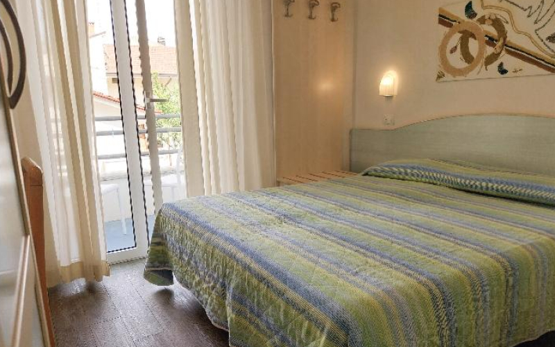 Helles Zimmer mit Doppelbett und grün gestreiftem Bettüberwurf.